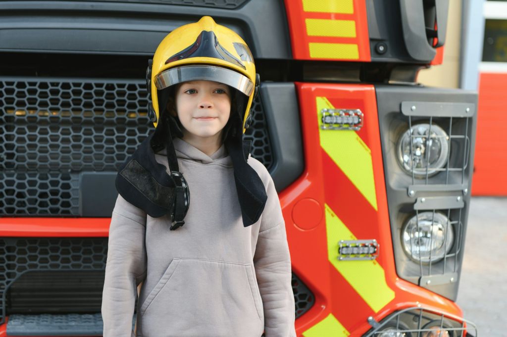 A boy wearing a fireman's helmet near a fire truck.